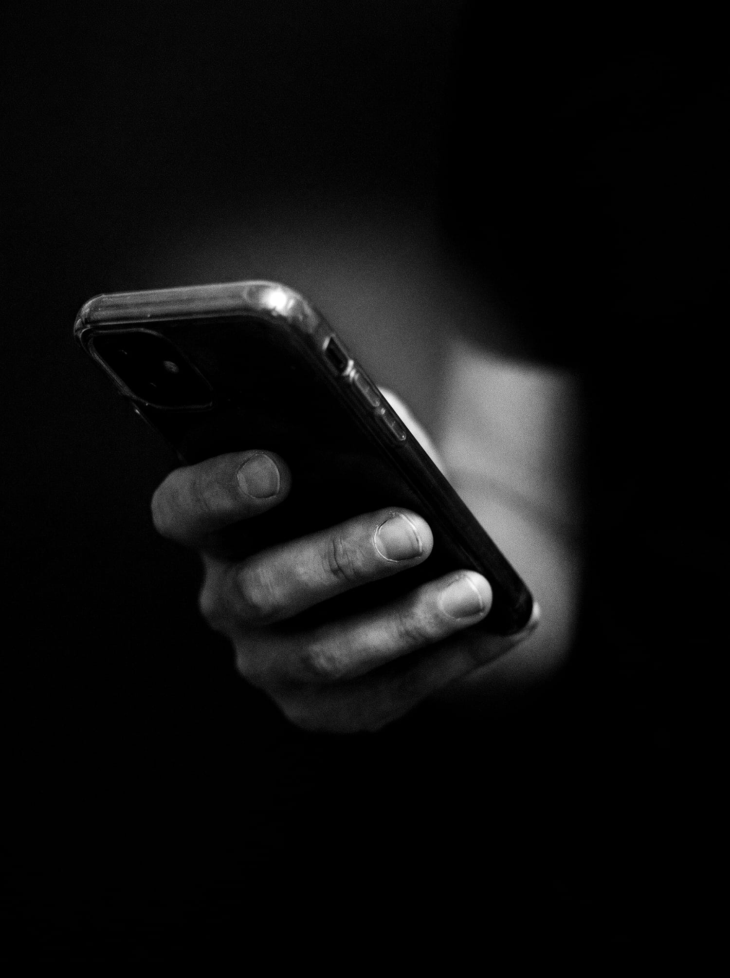 A hand holding a phone in a dark room, only the fingertips lit by the screen.